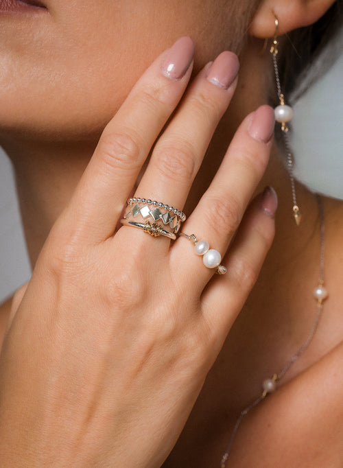 Close-up of a hand wearing a gold pearl ring with matching earring, sterling silver and gold stacking rings