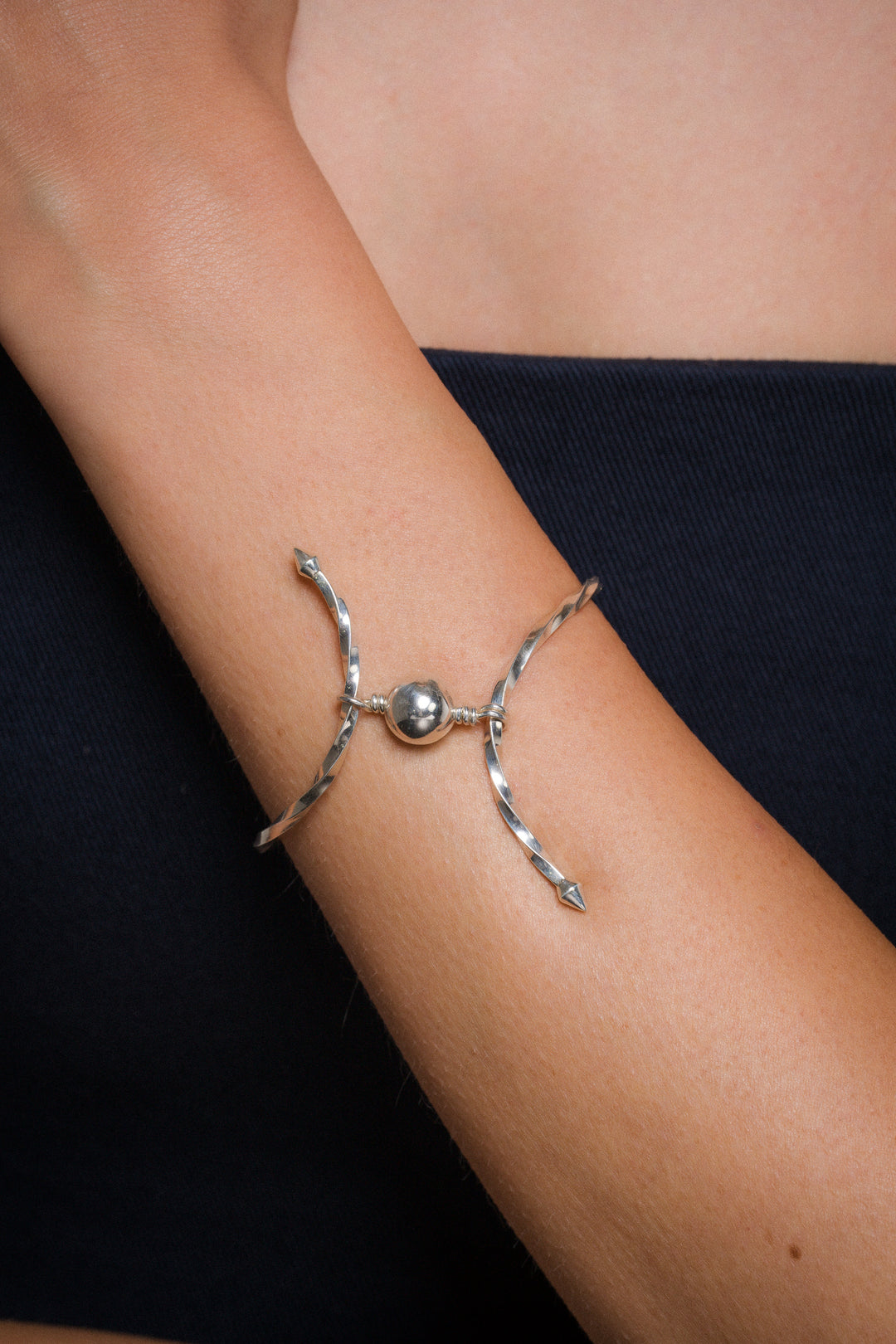 Silver bracelet with a central bead on a person's wrist against a dark background