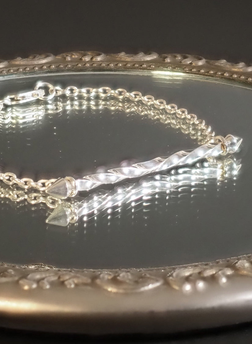 Silver bracelet with a twisting pendent on a reflective surface