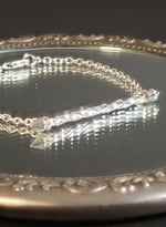 Load image into Gallery viewer, Silver bracelet with a twisting pendent on a reflective surface
