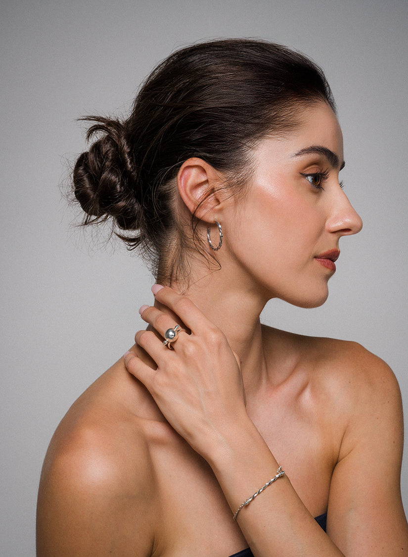 Woman with a stylish hair bun, wearing Illusion earrings and a ring, against a neutral background