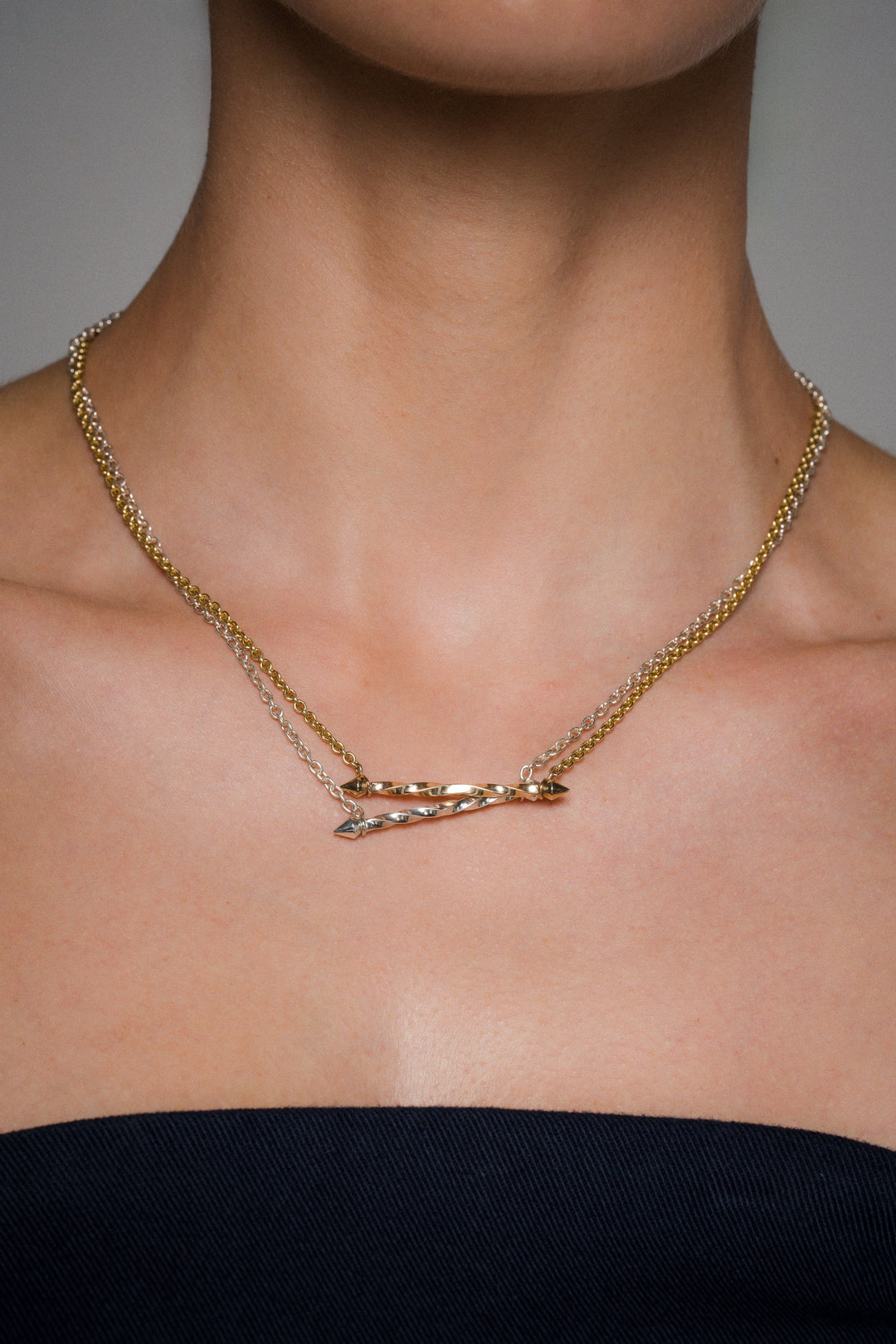 Gold necklace with a unique design on a person's neck against a neutral background