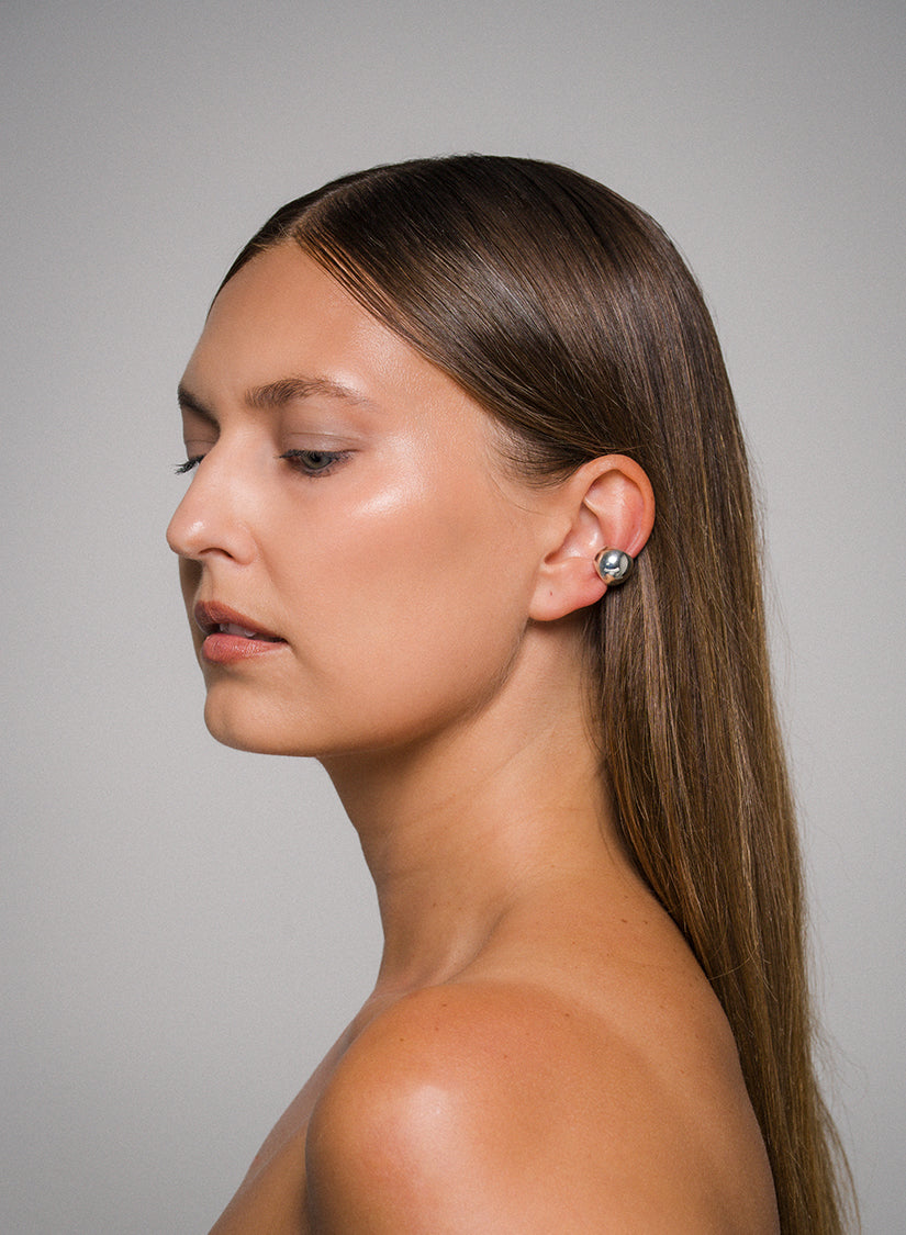 Side profile of a woman with long brown hair wearing a sculptural sterling silver ear cuff