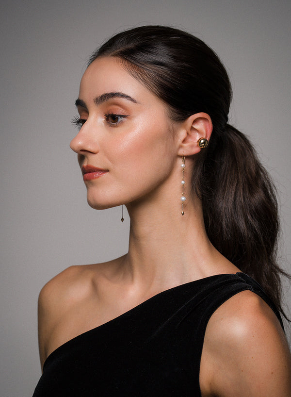 Woman wearing a black dress with pearl drop earrings.